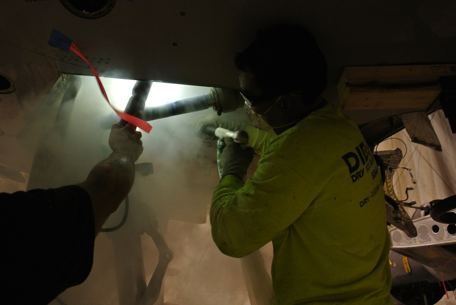 Dibshawaii technicians dry ice blasting the underside of an aircraft panel in a lit containment