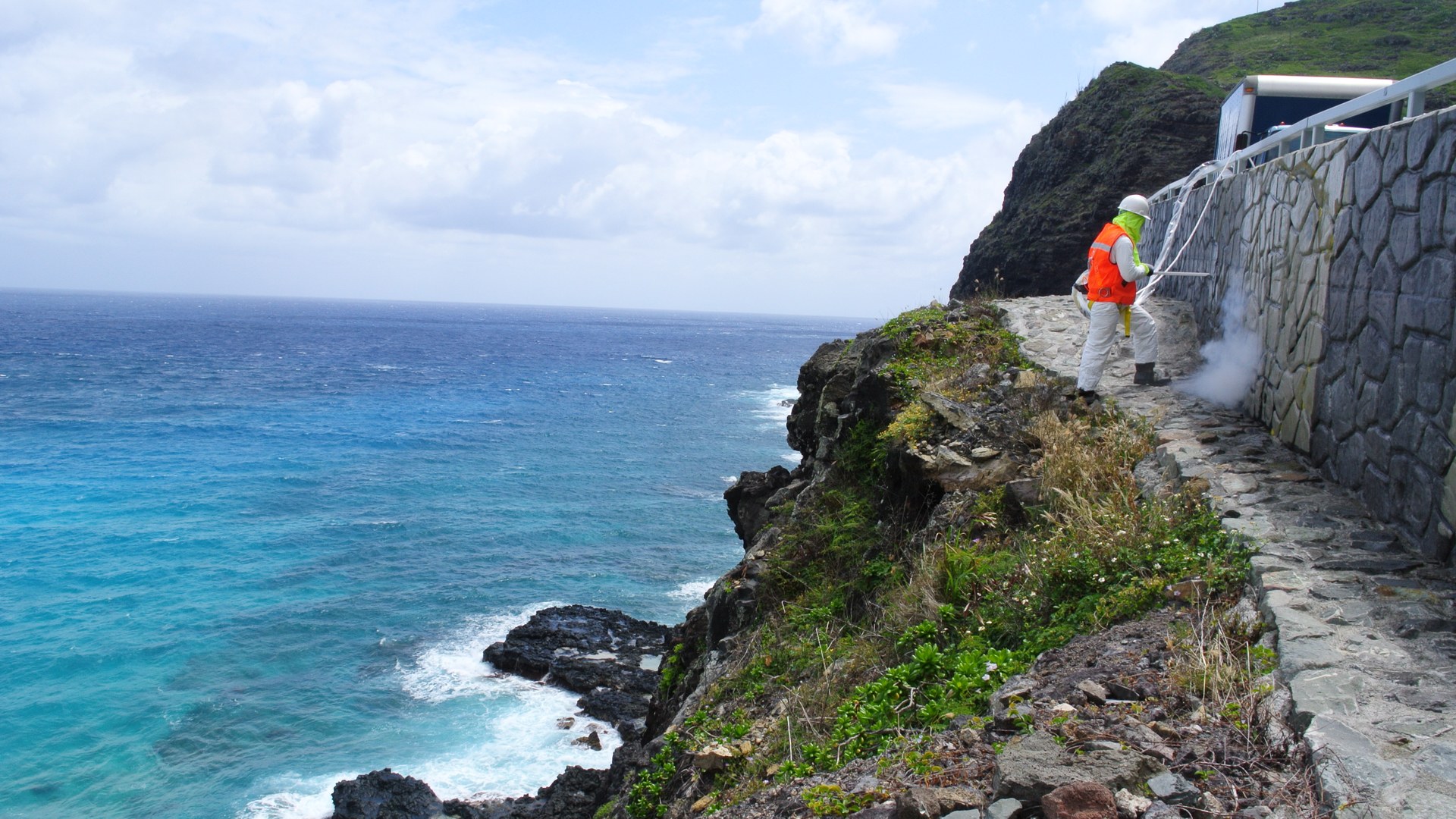 Dibshawaii technician dry ice blasting a seawall on a Hawaiʻi coastline above turquoise ocean